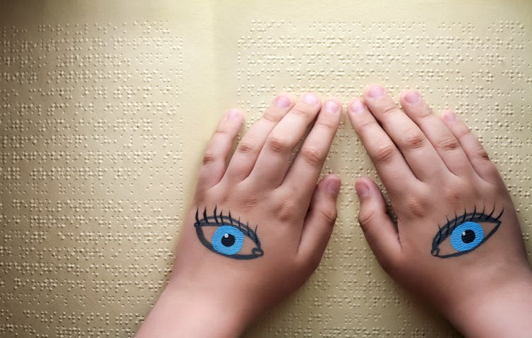 Unas manos con ojos pintados se deslizan sobre un texto en Braille.