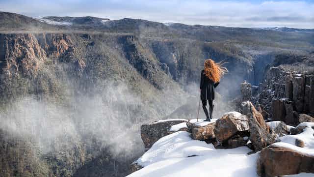 A woman stands on a snow capped ledge above a Tasmanian gully.