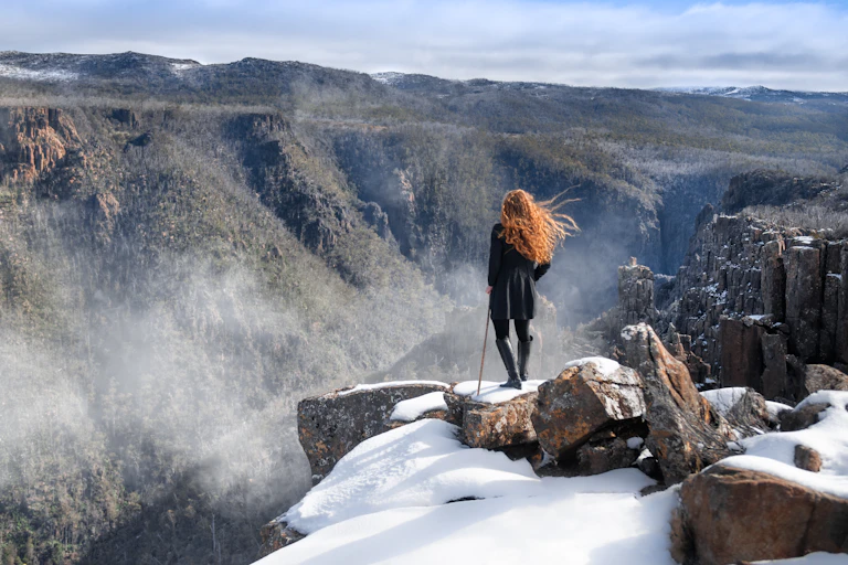 A woman stands on a snow capped ledge above a Tasmanian gully.