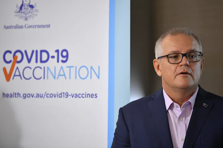 Prime Minister Scott Morrison stands in front of a sign reading 'COVID-19 Vaccination'.