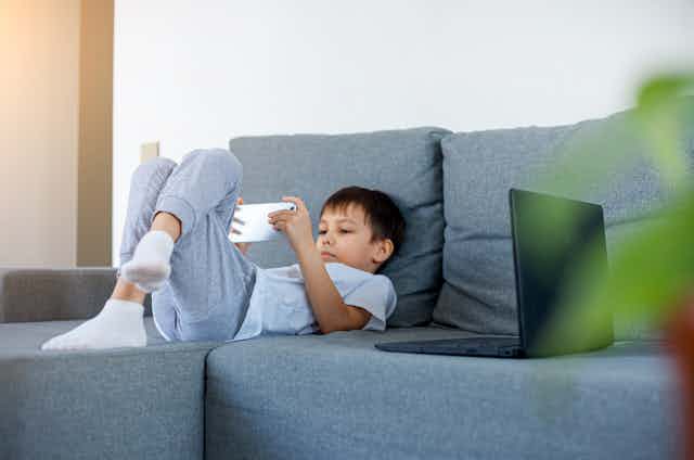 Boy watching something on phone on the couch.