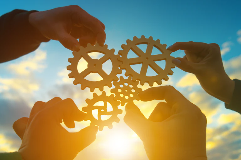 Four hands holding shapes of machine cogs fitting together