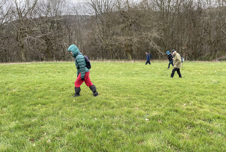 Four people walking in a line in a field.