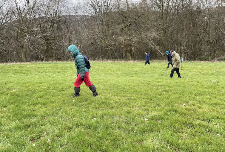 Four people walking in a line in a field.