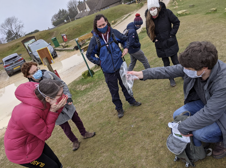 A group of people standing watching one person show the other a meteorite in a bag.