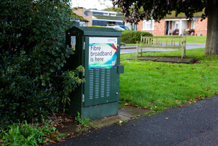 A green internet cabinet on a grassy verge next to a pavement.