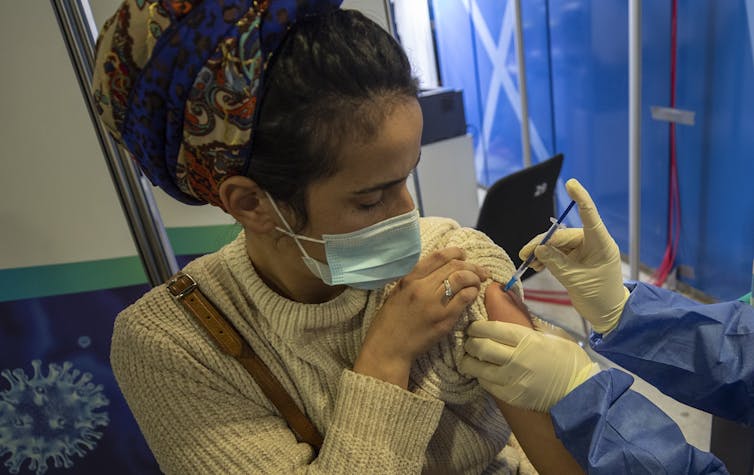 A woman with a facemask receives an injection