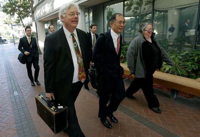Six people in business attire carrying briefcases walk along a sidewalk