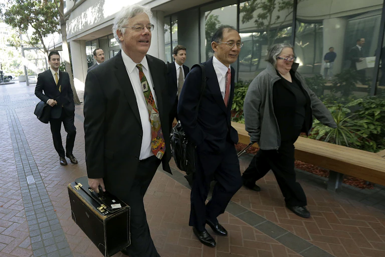 Six people in business attire carrying briefcases walk along a sidewalk