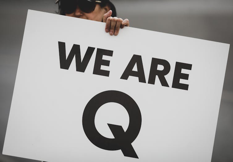 Woman holding up a sign that reads 'We are Q'