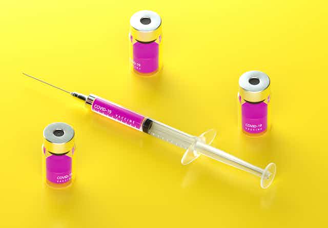 A syringe sitting next to vials of vaccine.