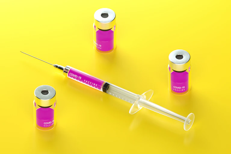 A syringe sitting next to vials of vaccine.
