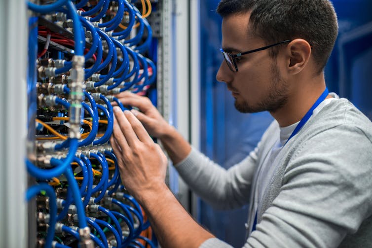 A man connects wires into the back of a computer.