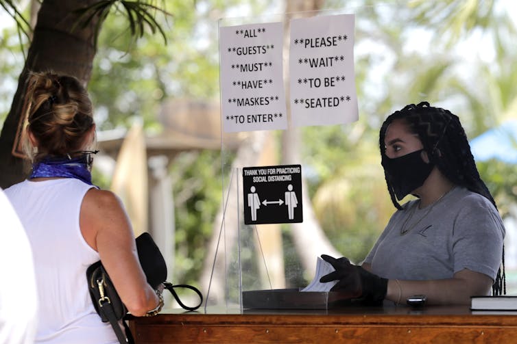 A woman worker wearing a mask waits for a customer whose face is turned away to order at a cafe.