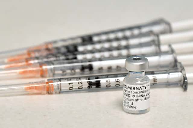 A vial of the Pfizer vaccines, with several syringes next to it.