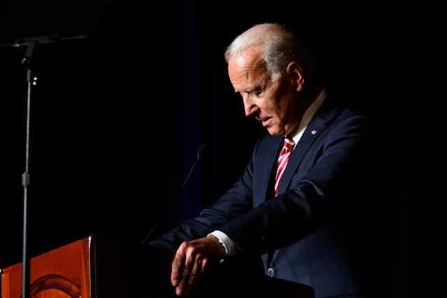 Joe Biden at a lectern with his head bowed