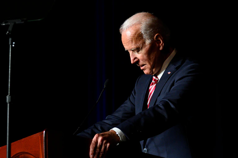 Joe Biden at a lectern with his head bowed
