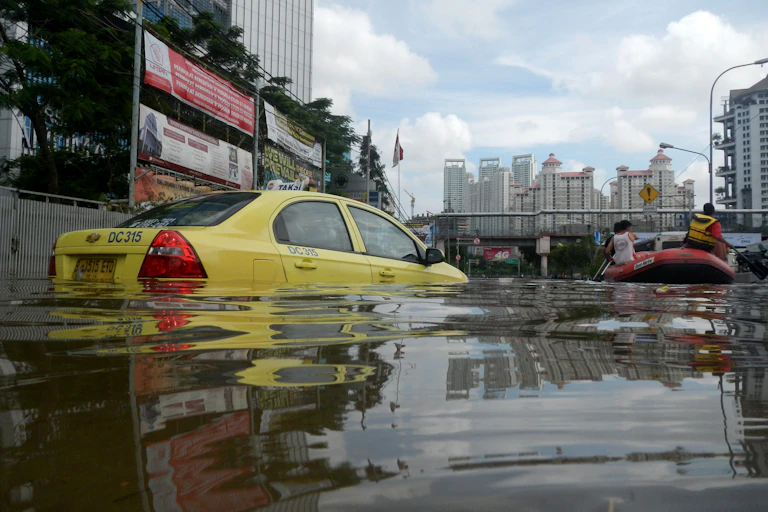 A yellow taxi on flooded street, large buildings in background
