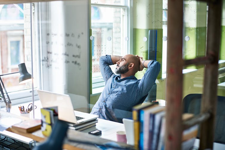 A man leans back from his desk