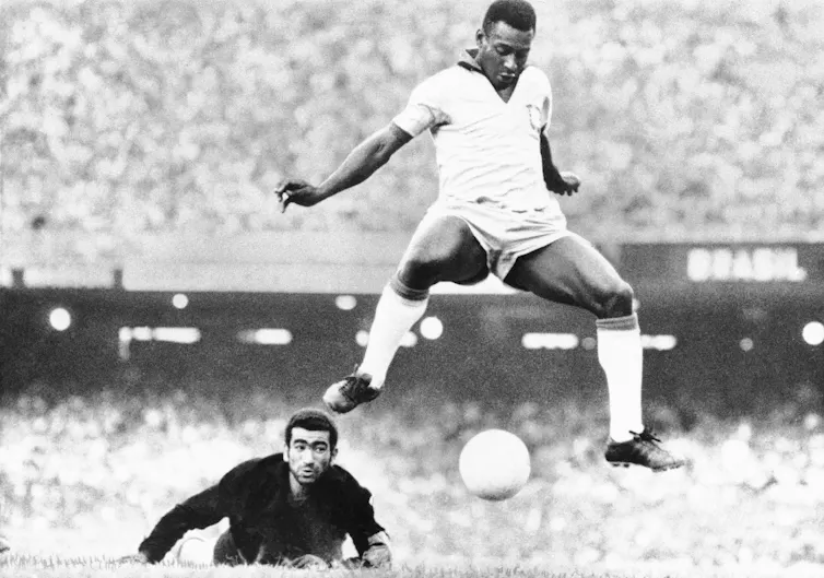 Soccer player is seen mid-air, ball between his feet.