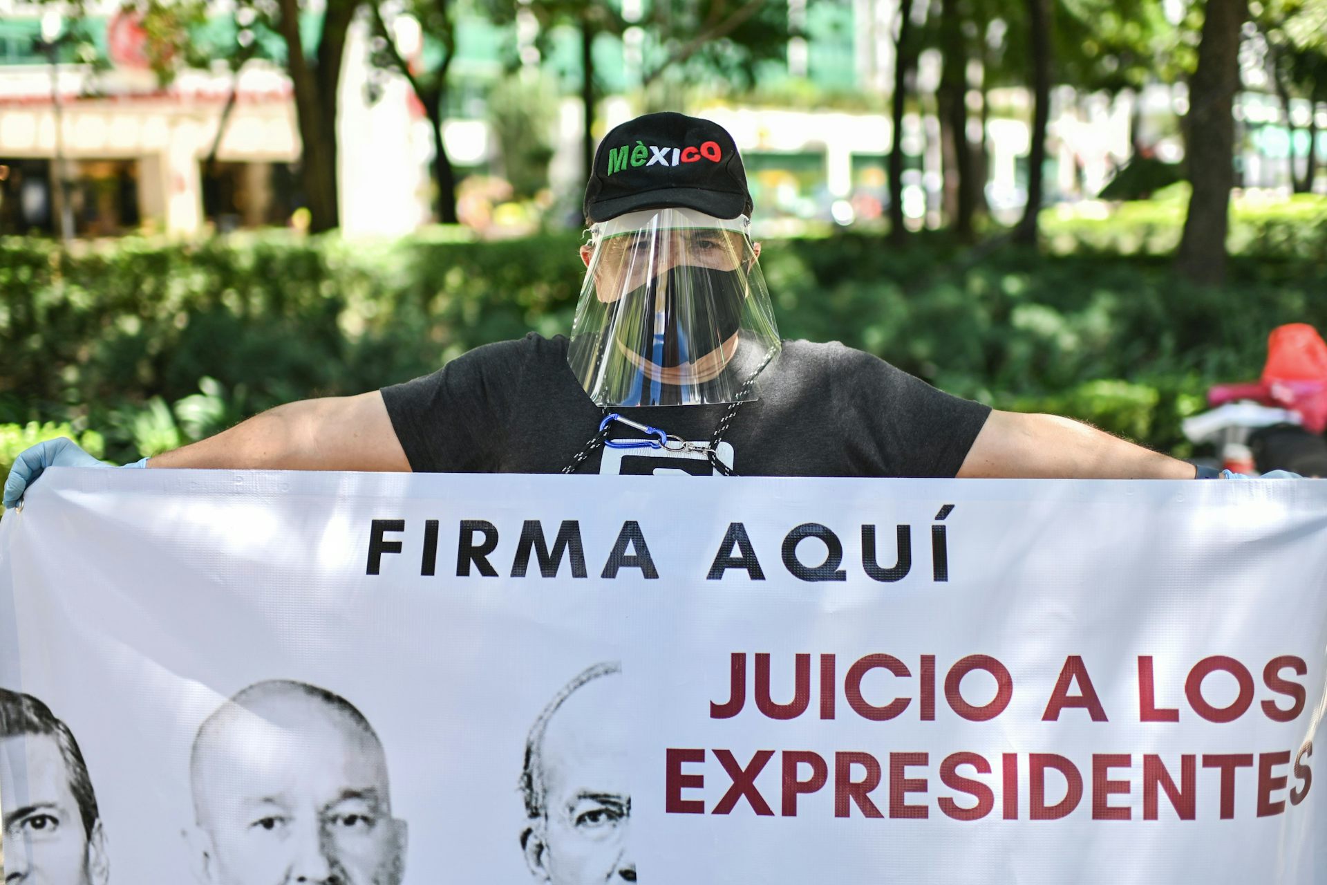 Man in face mask and face shield holds a sign reading 'trials for ex-presidents - sign here'