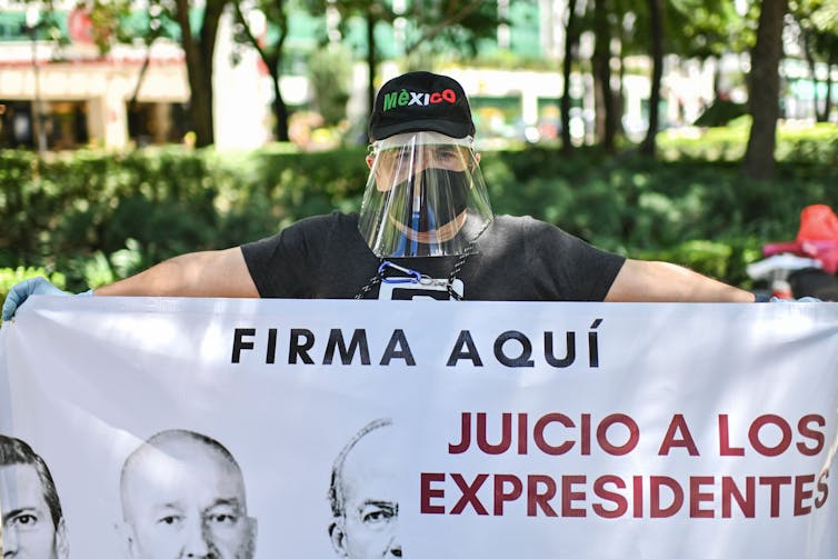 Man in face mask and face shield holds a sign reading 'trials for ex-presidents – sign here'