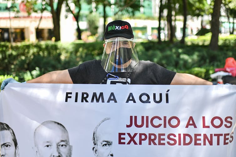 Man in face mask and face shield holds a sign reading 'trials for ex-presidents - sign here'