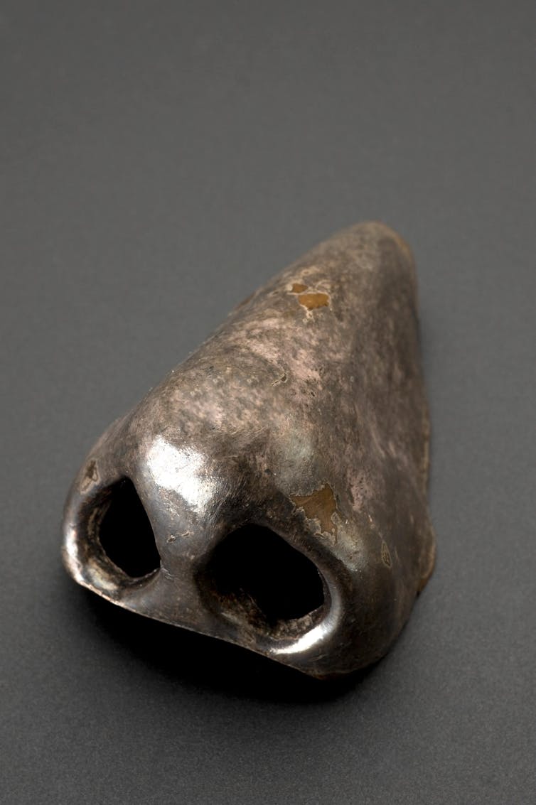 Silver coloured artificial nose on grey background.