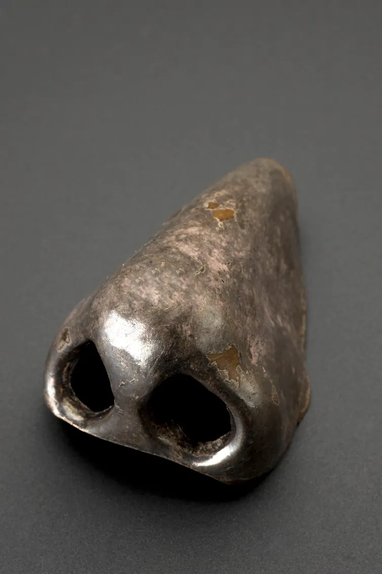 Silver coloured artificial nose on grey background.
