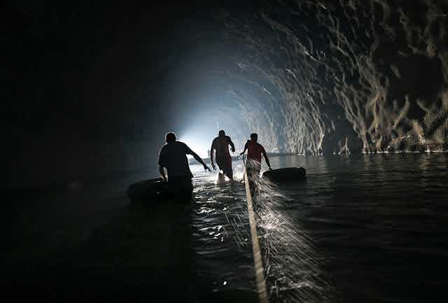 Three men walk through a dark tunnel