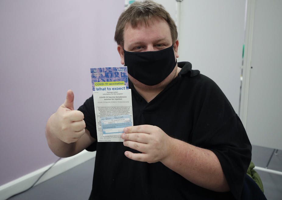 A man weaing a mask gives a thumbs up while holding up a leaflet on COVID-19 