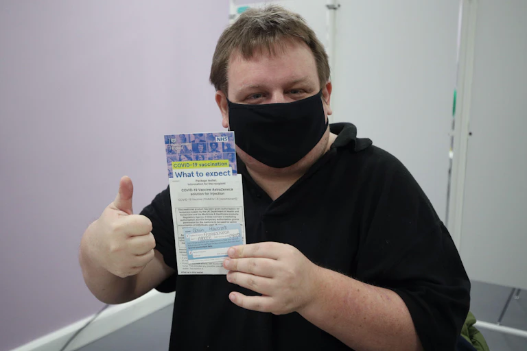 A man weaing a mask gives a thumbs up while holding up a leaflet on COVID-19
