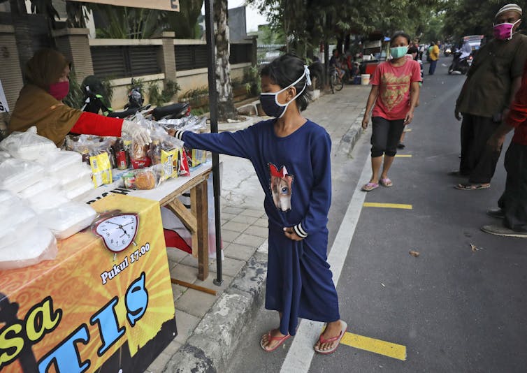 Girl in Indonesia wearing mask and reaching for food in a market stall.