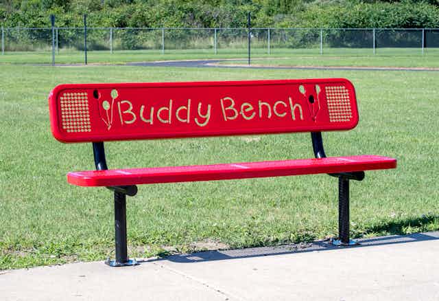 A red buddy bench in school field.