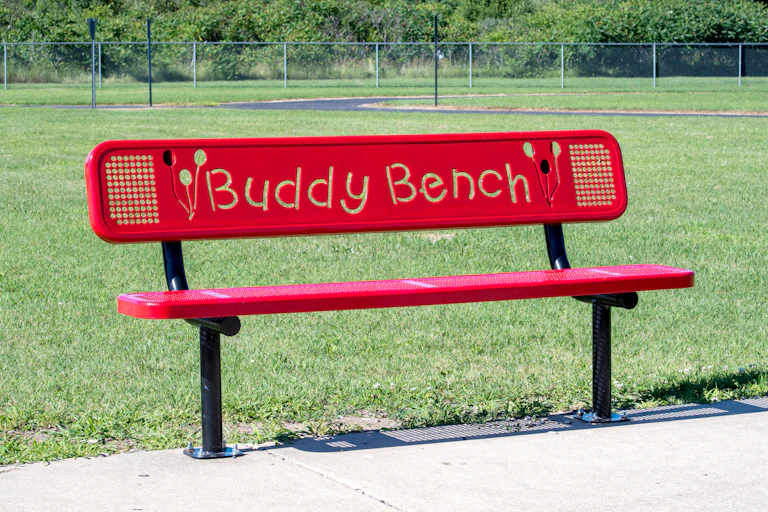 A red buddy bench in school field.