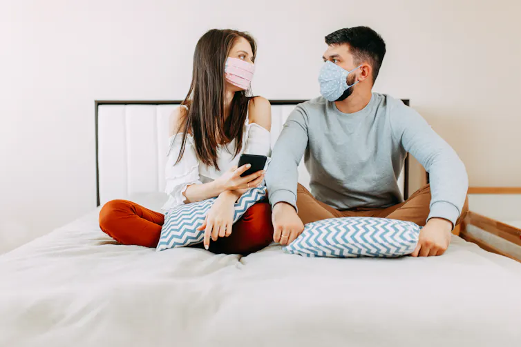 A couple on a bed wearing surgical face masks