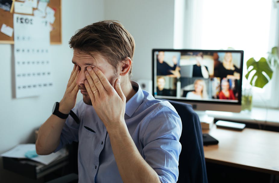 A man rubbing his eyes facing away from a computer screen with six people on a video call.