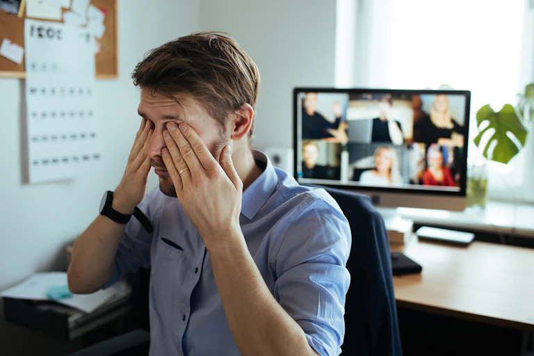 A man rubbing his eyes facing away from a computer screen with six people on a video call.