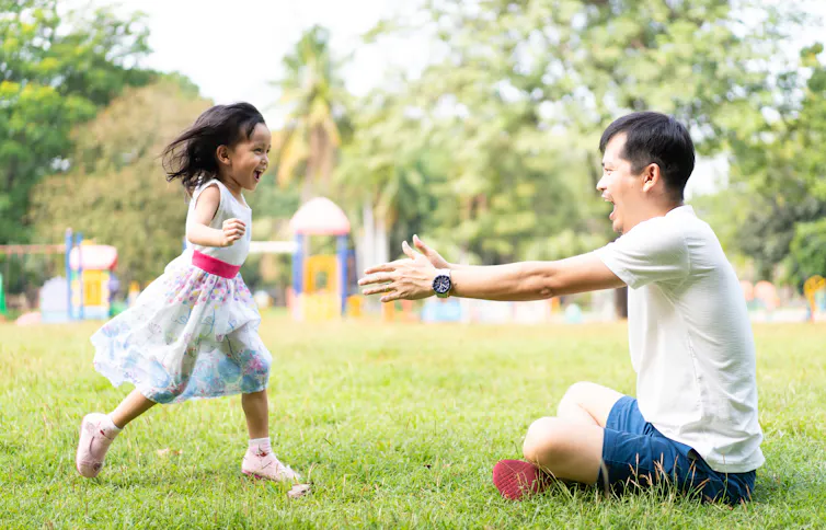 little girl wearing a dress running to man with open arms in park