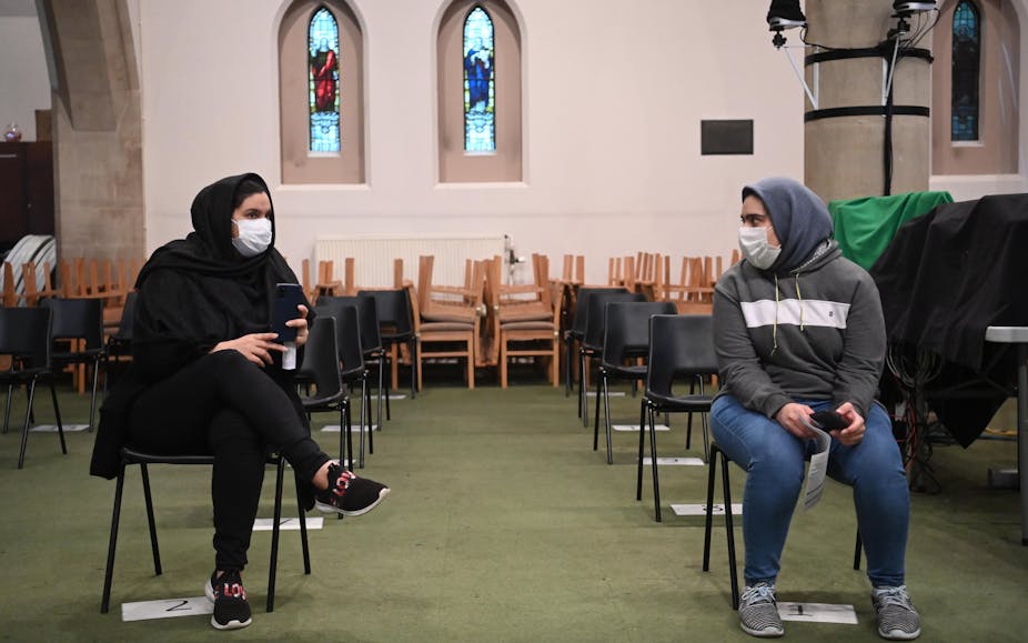 Two women wearing masks wait to have their vaccine in a church.