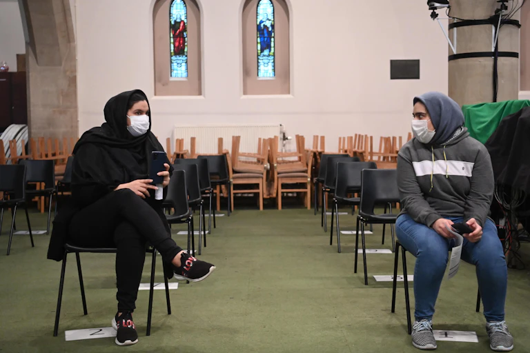 Two women wearing masks wait to have their vaccine in a church.