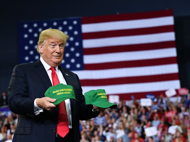 Trump at a rally throwing MAGA hats into a crowd.