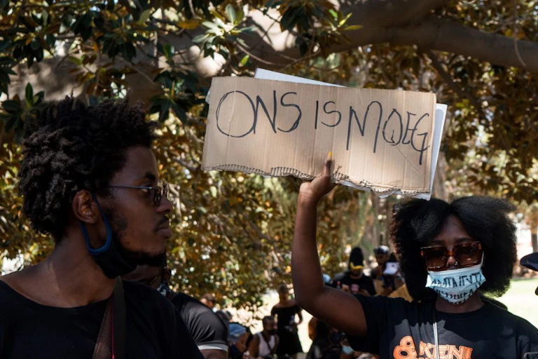 A woman wearing a white COVID-19 mask raises a protest placard while a man looks on.