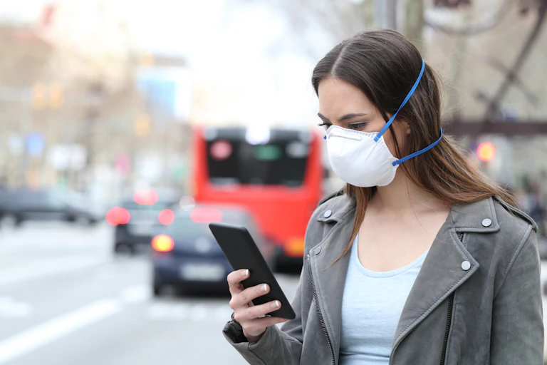 A woman in a mask outside, checking her phone