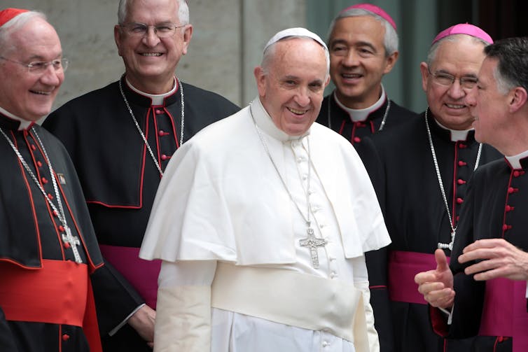 Pope Francis surrounded by bishops in red.