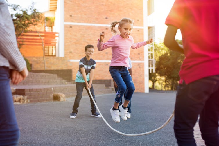 Kids playing jump rope with teacher watching.