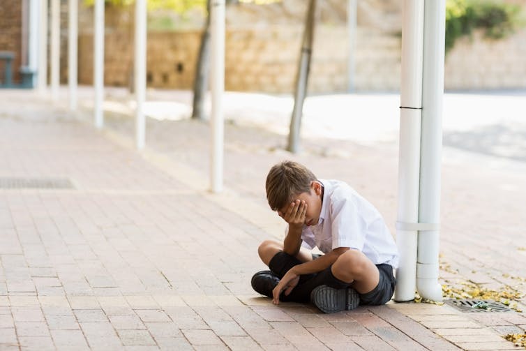 Sad schoolboy sitting on the ground with head in hands.