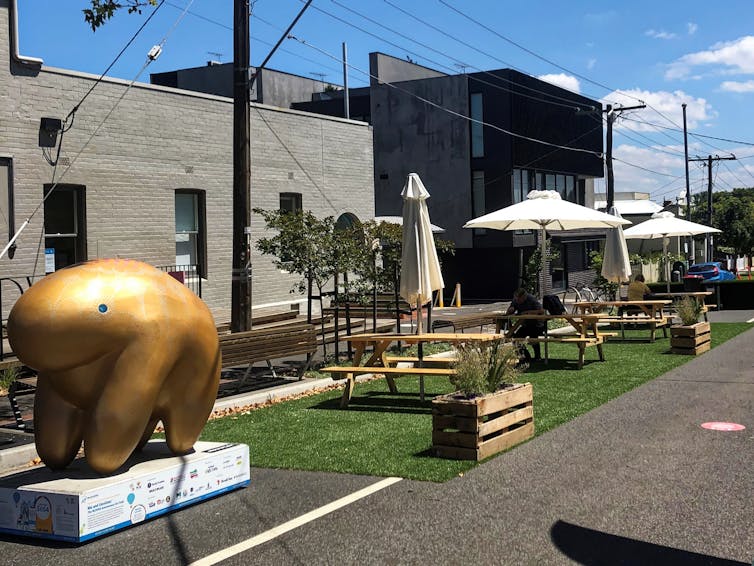 streetside pop-up parklet with artificial grass, potted plants, tables and chairs