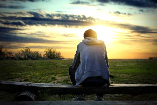 Young man sitting on fence and watching sunset.
