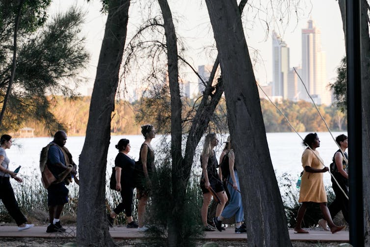 People walk alongside lake, city buildings